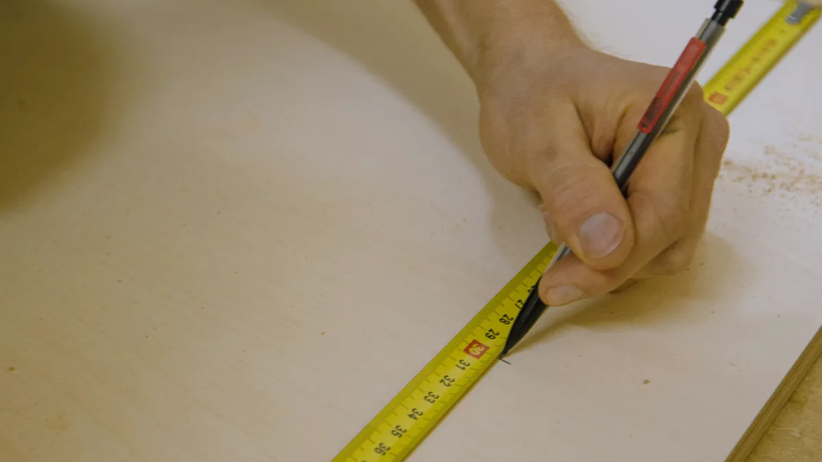 Carpenter marking a measurement on a plywood sheet with a pencil and tape measure