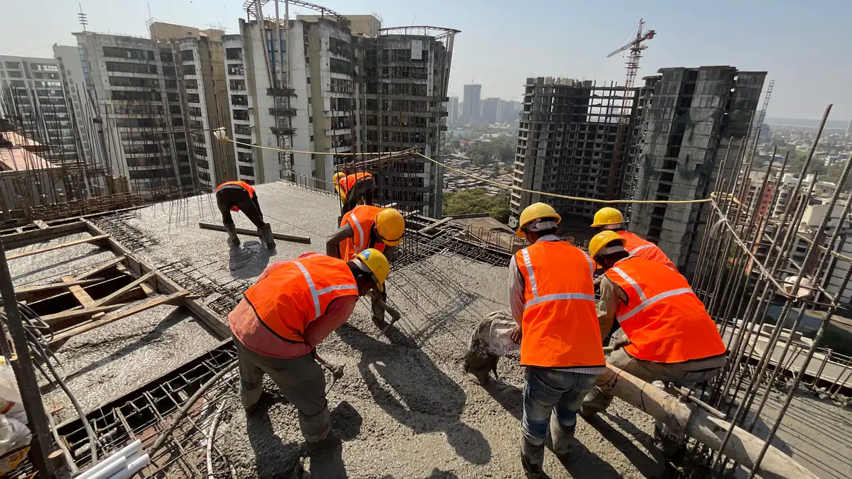Workers in safety vests placing concrete on a high-rise slab at a construction site in India, with timber shuttering at the slab edge