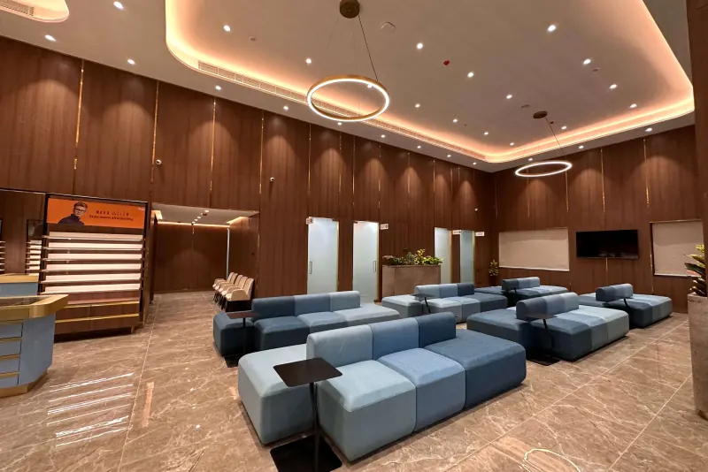 Patient waiting lounge with blue modular seating, timber wall panelling and a cove-lit ceiling at the Dr Agarwal Eye Hospital, Kolkata